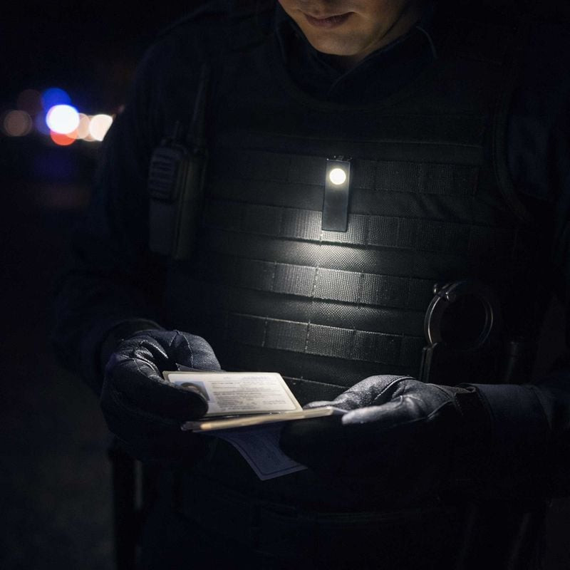Lampe LED mini Patrol 1047974 clipsée sur gilet policier la nuit, illuminant documents tenus par off