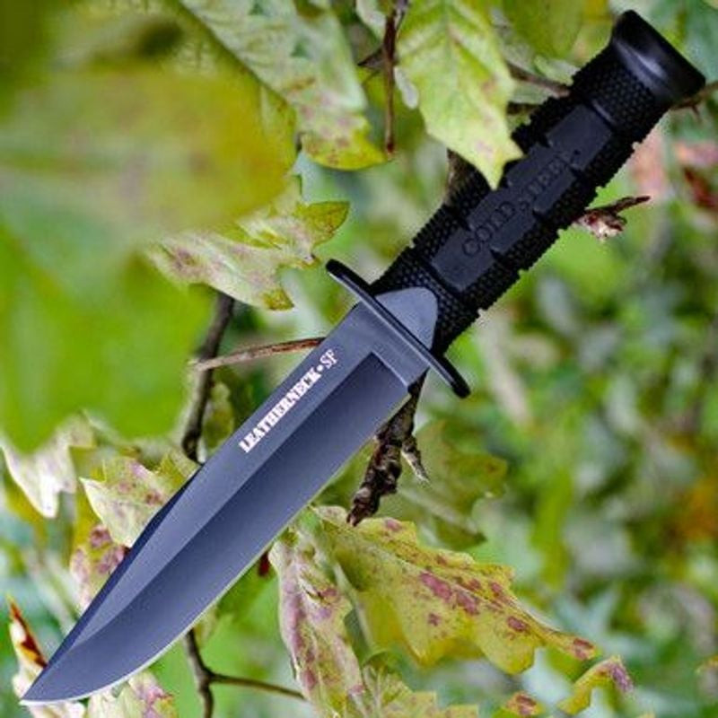Poignard Cold Steel Leatherneck SF en cadre naturel, lame et manche noirs sur fond de feuilles verte