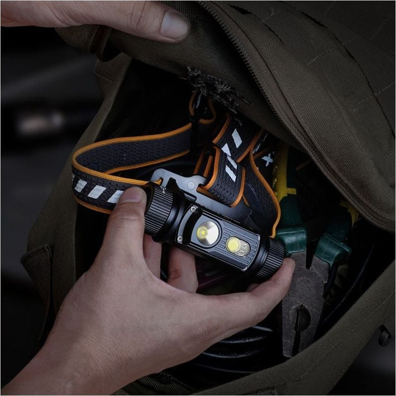 Personne portant la lampe frontale Fenix HM70R dans une forêt de nuit, avec un puissant faisceau lum